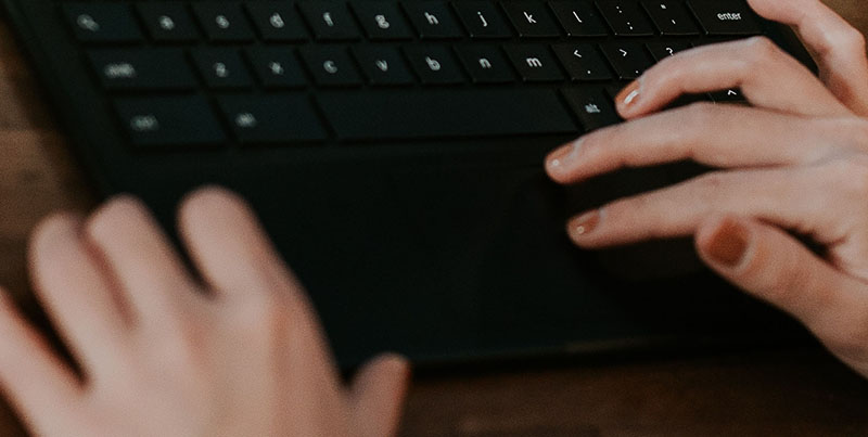woman's hands using the trackpad on a black laptop